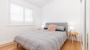 Ein Schlafzimmer mit einem Bett, zwei Nachttischen, einem Fenster mit Jalousien und einer Tür.