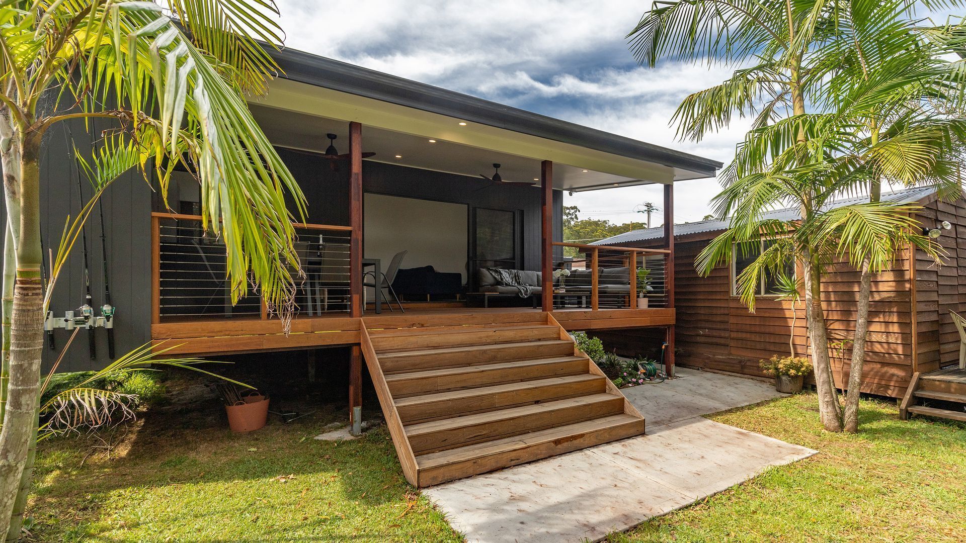 Une maison moderne dotée d’une terrasse en bois, d’un espace salon extérieur abrité et d’un petit jardin.