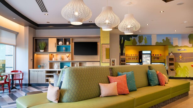 A modern living area with a green sofa, red chairs, and pendant lighting. - Home2 Suites By Hilton Atlanta Airport College Park (College Park)