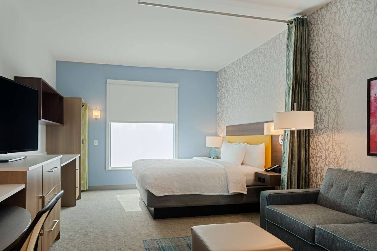 Ein Hotelzimmer mit Bett, Schreibtisch, Fernseher, Sofa und einem Fenster mit Vorhängen.