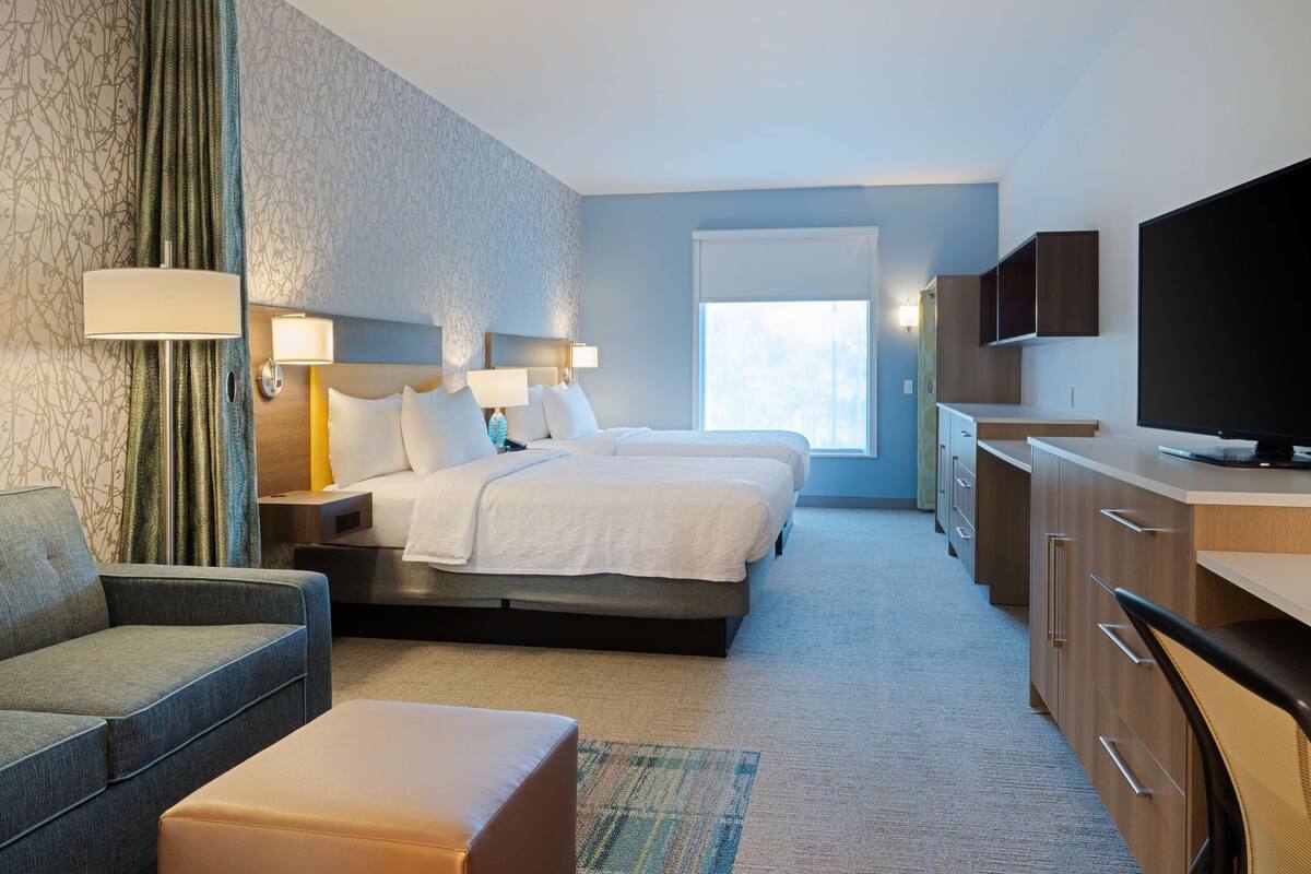 Ein Hotelzimmer mit zwei Betten, einem Sofa, einem Fernseher und einem Schreibtisch.
