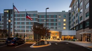 A modern hotel with a prominent American flag, a parking area, and a well-lit entrance. - Home2 Suites By Hilton Atlanta Airport College Park (College Park)