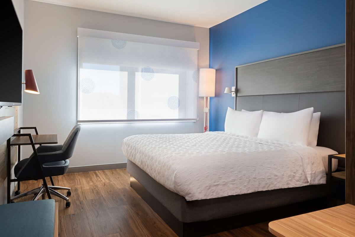 Ein modernes Hotelzimmer mit einem großen Bett, einem Schreibtisch, einem Stuhl und einem Fenster mit Blick.