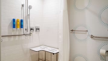 A modern bathroom with white subway tiles, a shower with a handheld showerhead, a grab bar, and a small table with a towel.
