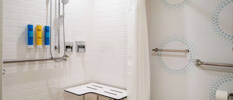 A modern bathroom with white subway tiles, a shower with a handheld showerhead, a grab bar, and a small table with a towel.