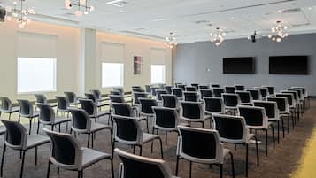 A conference room with rows of chairs, ceiling lights, and large windows.
