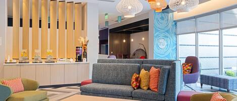 A modern lobby with a sofa, armchairs, a coffee station, and a reception desk.