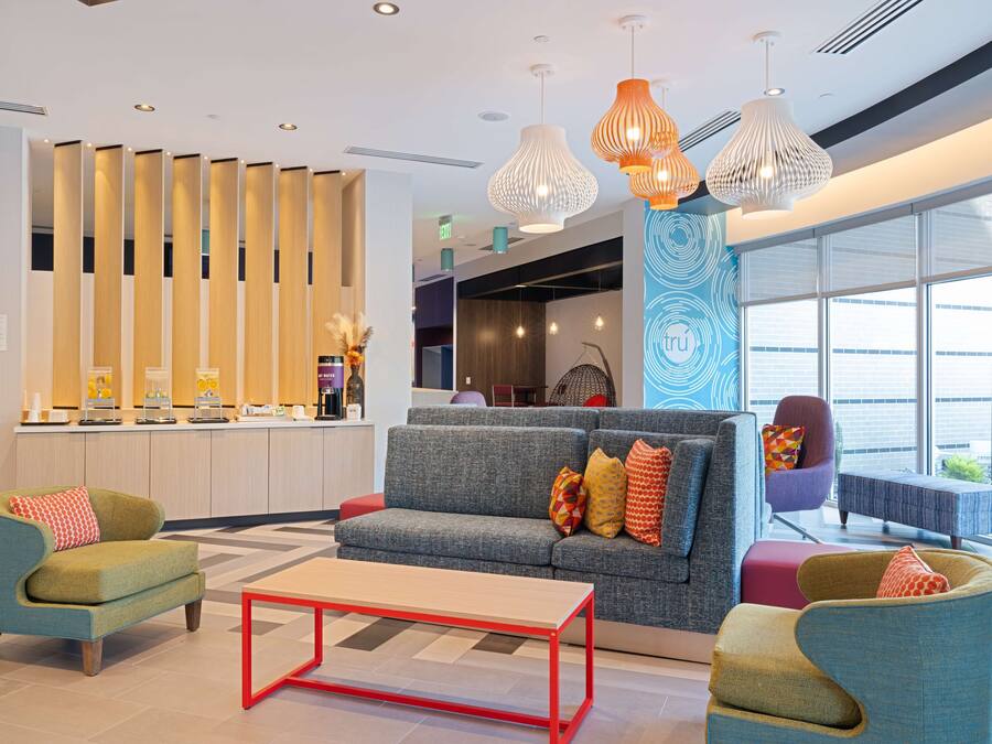 A modern lobby with a sofa, armchairs, a coffee station, and a reception desk.