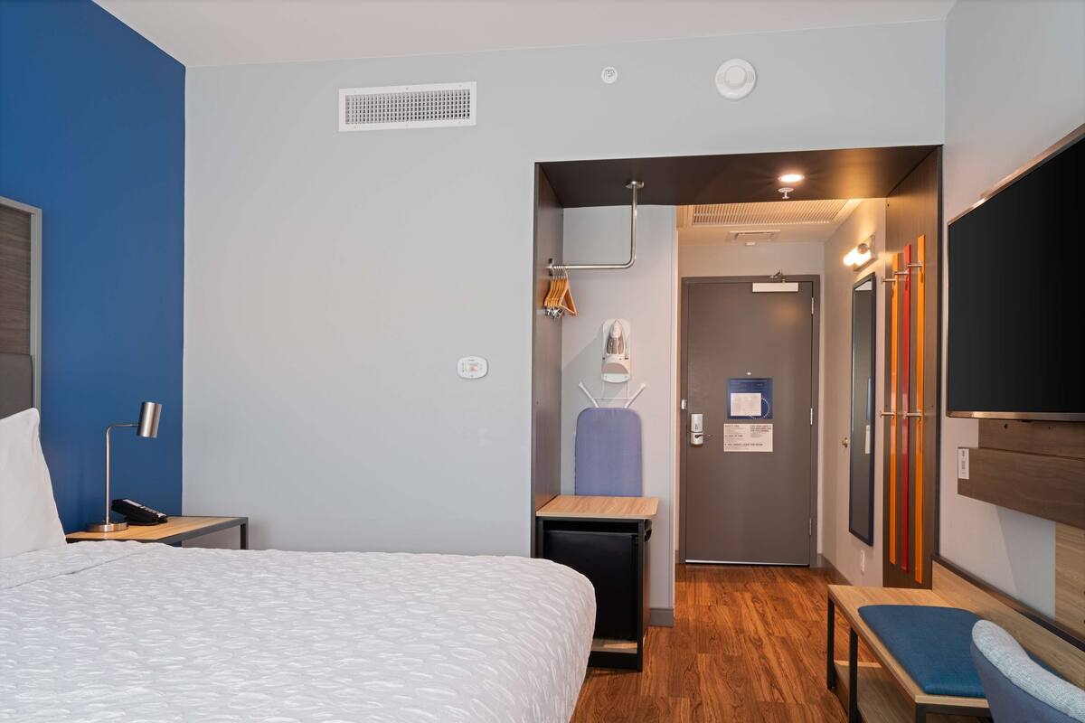 Ein modernes Hotelzimmer mit einem großen Bett, einem Schreibtisch, einem Stuhl, einem Spiegel und einem Kleiderschrank.