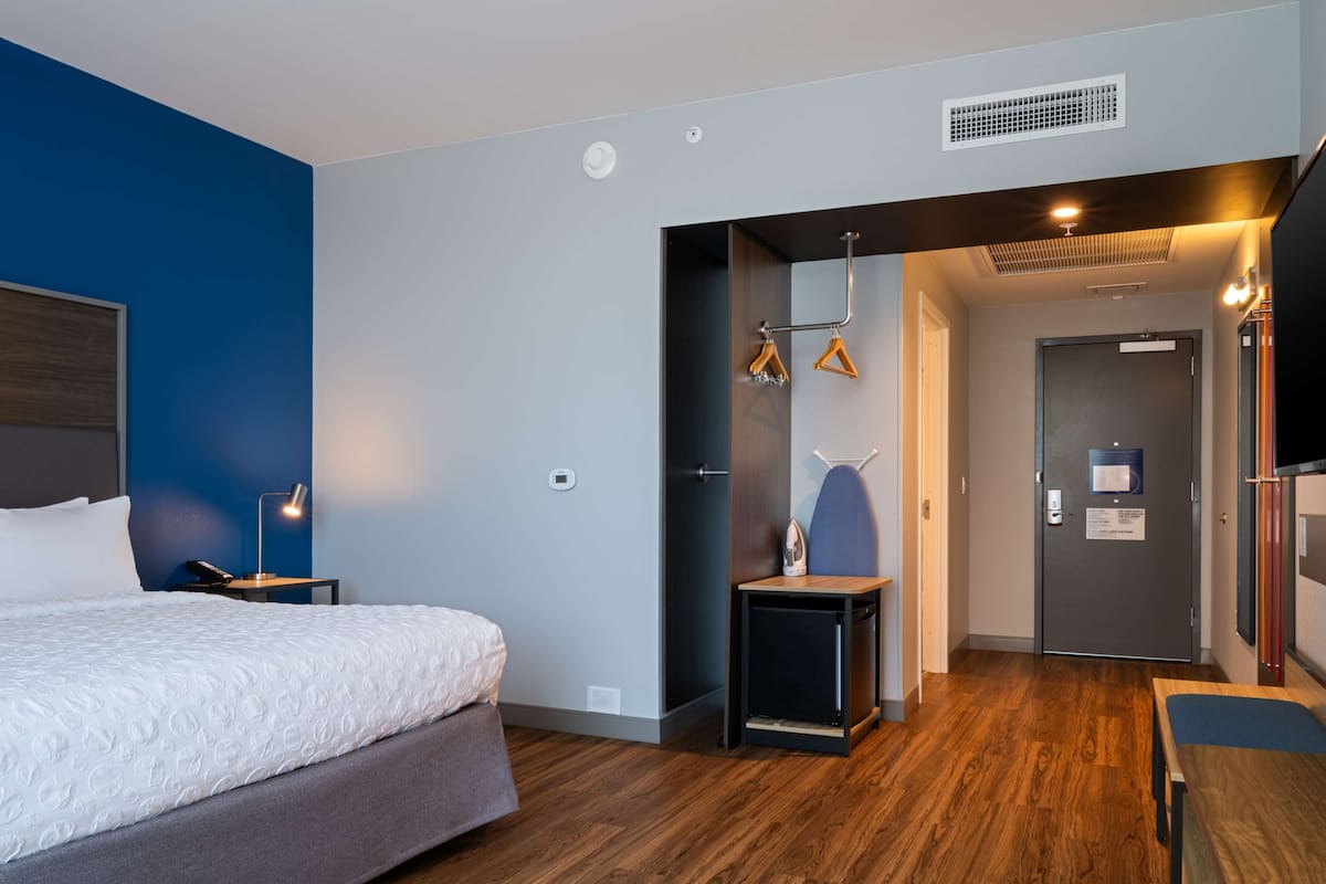 Ein modernes Hotelzimmer mit einem Bett, Nachttisch, Lampe und einem kleinen Tisch mit einem Bügeleisen.
