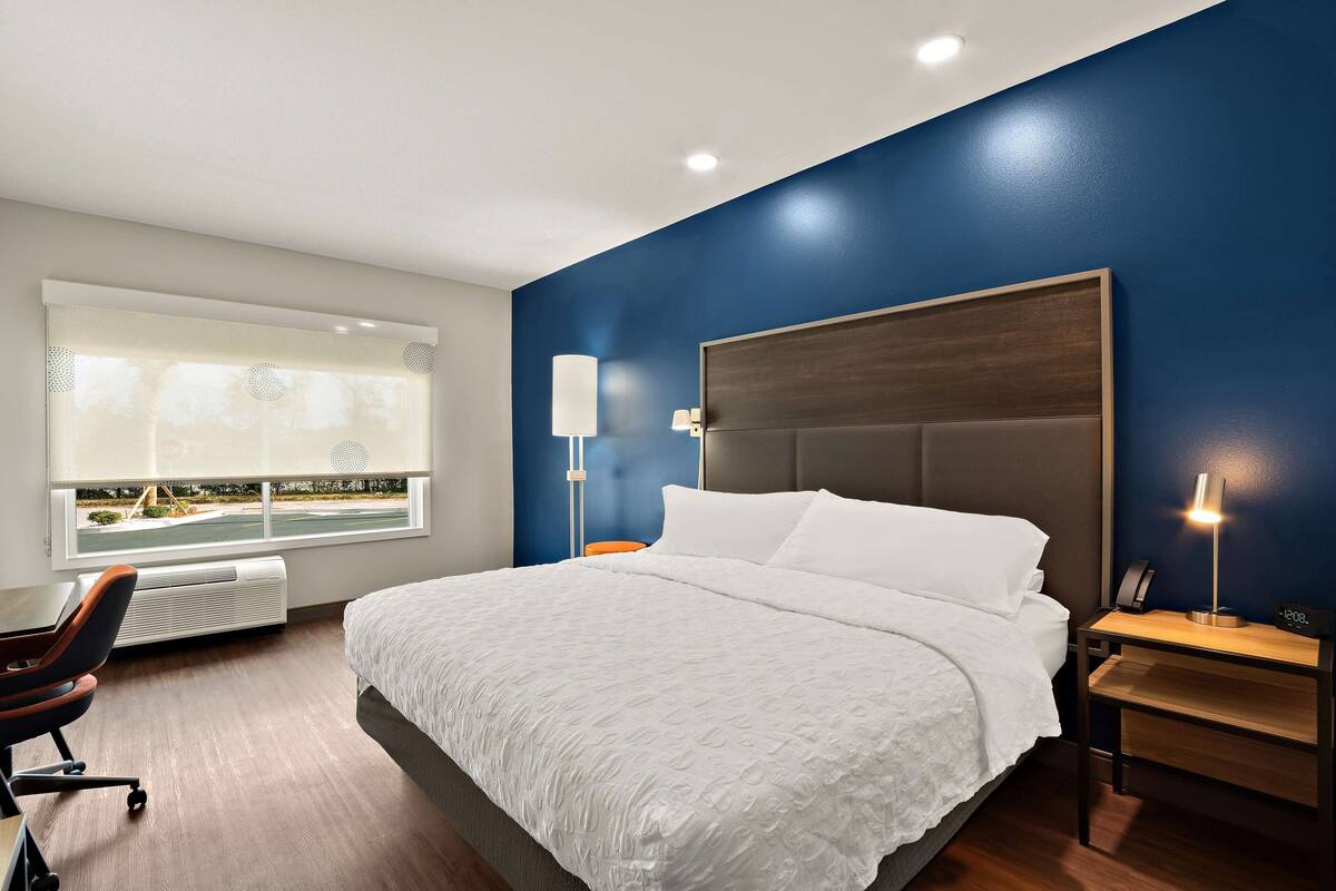A hotel room with a large bed, a desk with a chair, a nightstand, and a window with a view of a golf course.