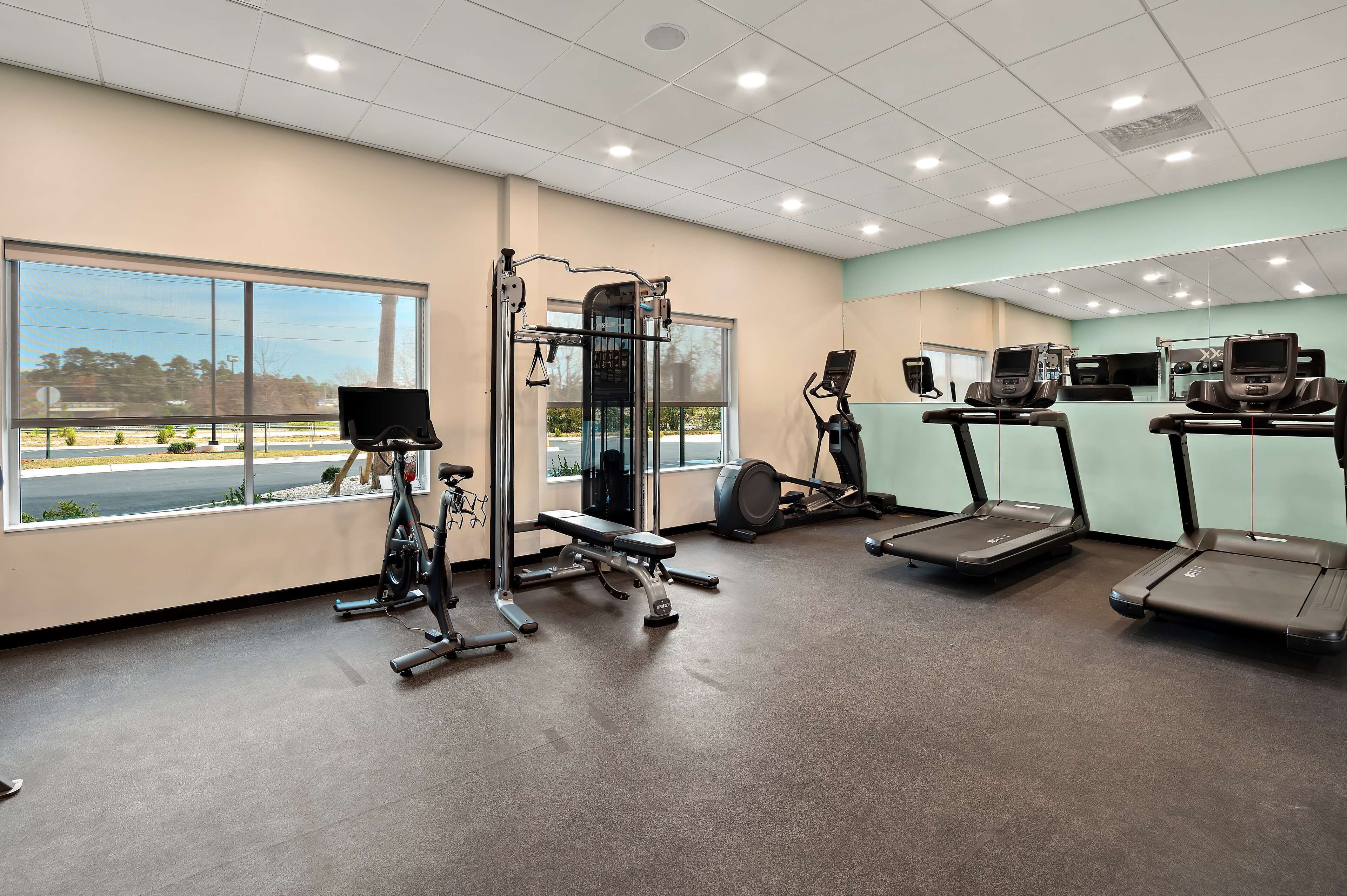 A gym with cardio machines, weightlifting equipment, and large windows offering a view of the outdoors.