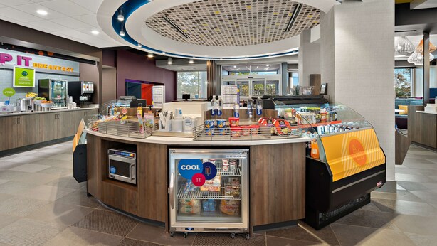 A breakfast area with a self-service counter, refrigerated display, and a digital menu board. - Tru By Hilton Santee (Santee)