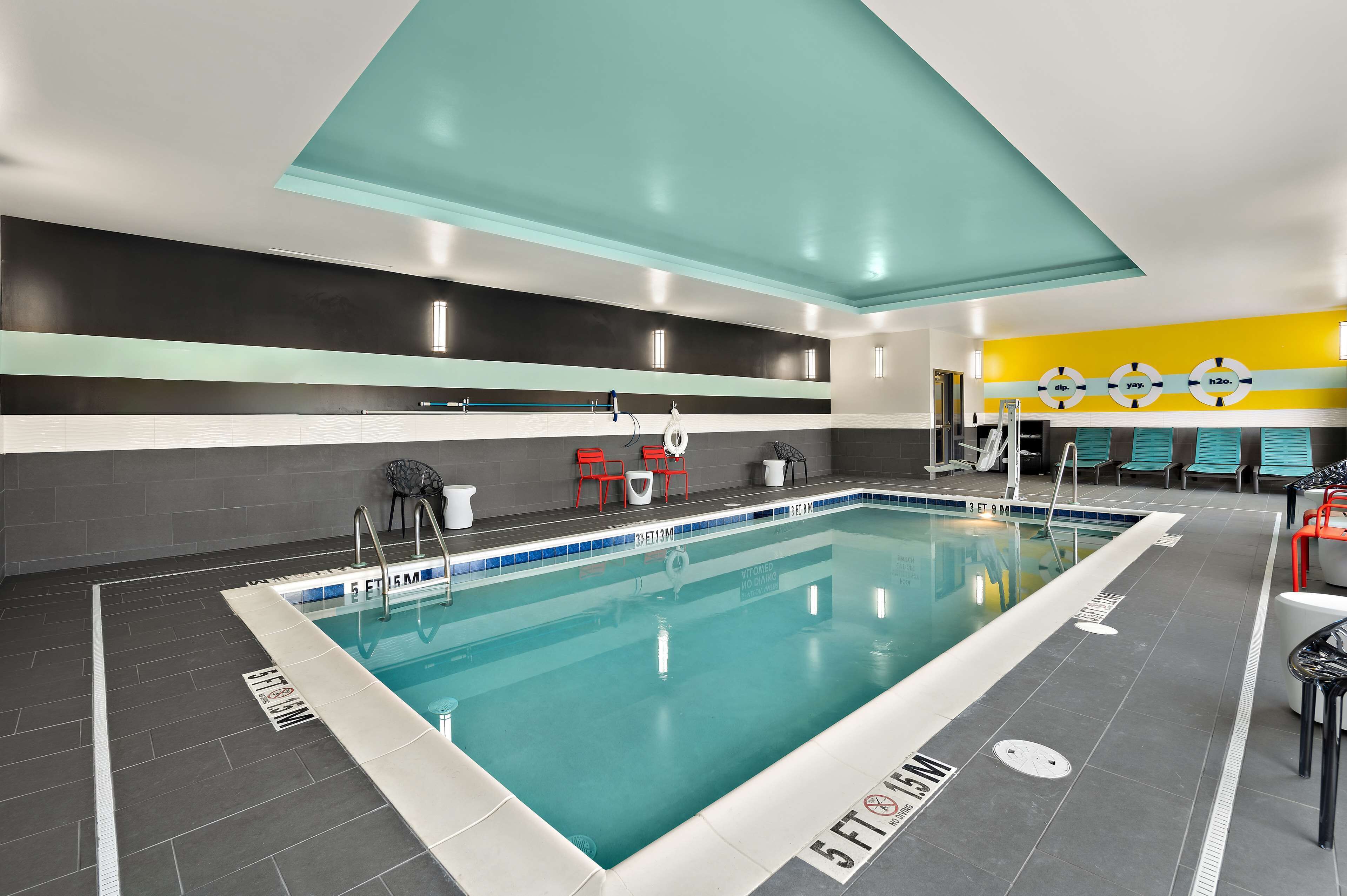 An indoor swimming pool with clear lane markings, a tiled floor, and a ceiling with a geometric design.