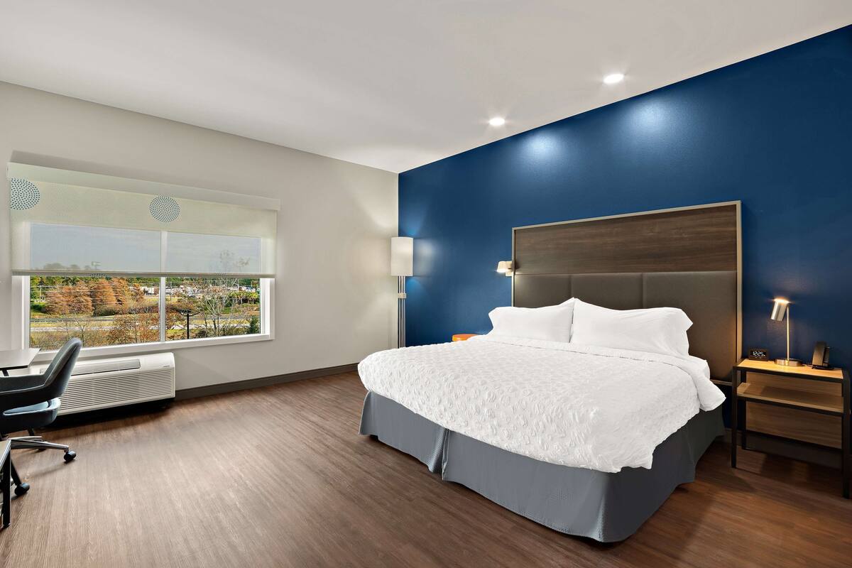 A modern hotel room with a large bed, a desk, and a window with a view of the outdoors.
