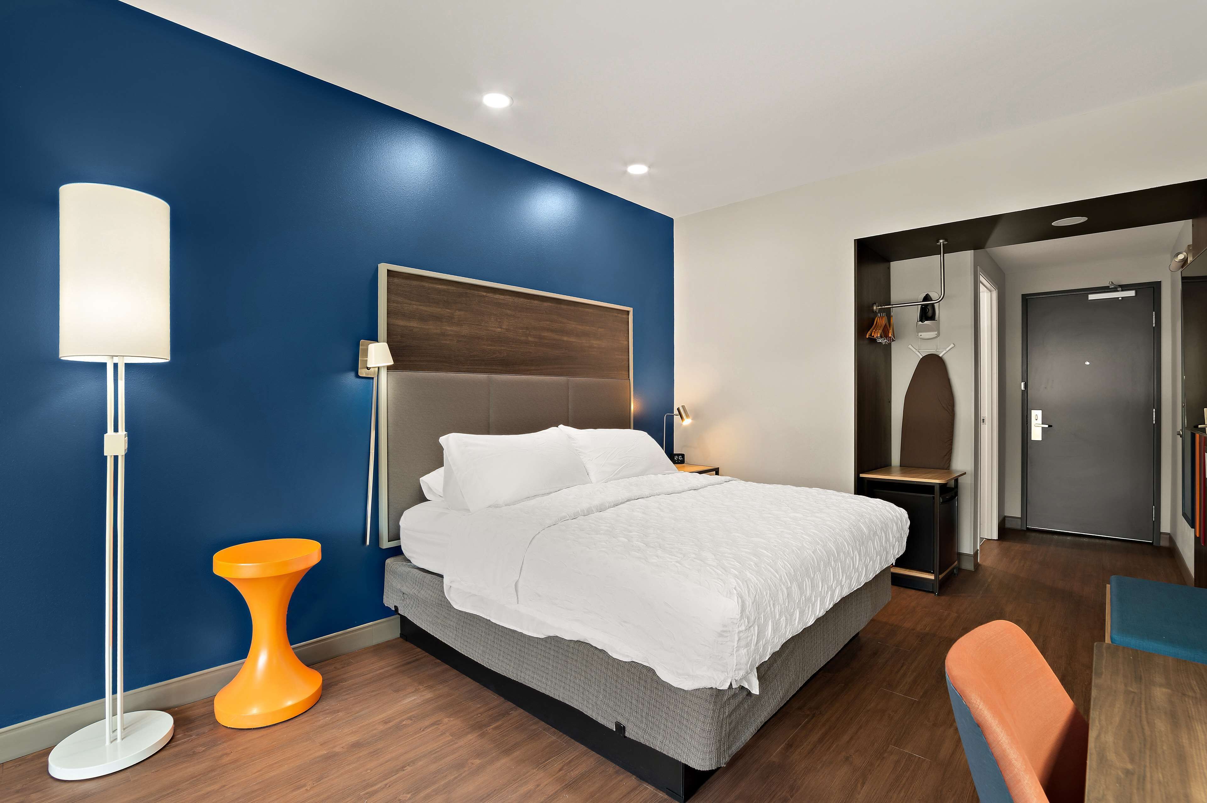 Ein modernes Hotelzimmer mit einem Bett, einer Stehlampe und einem kleinen orangefarbenen Tisch.