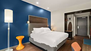 Ein modernes Hotelzimmer mit einem Bett, einer Stehlampe und einem kleinen orangefarbenen Tisch.