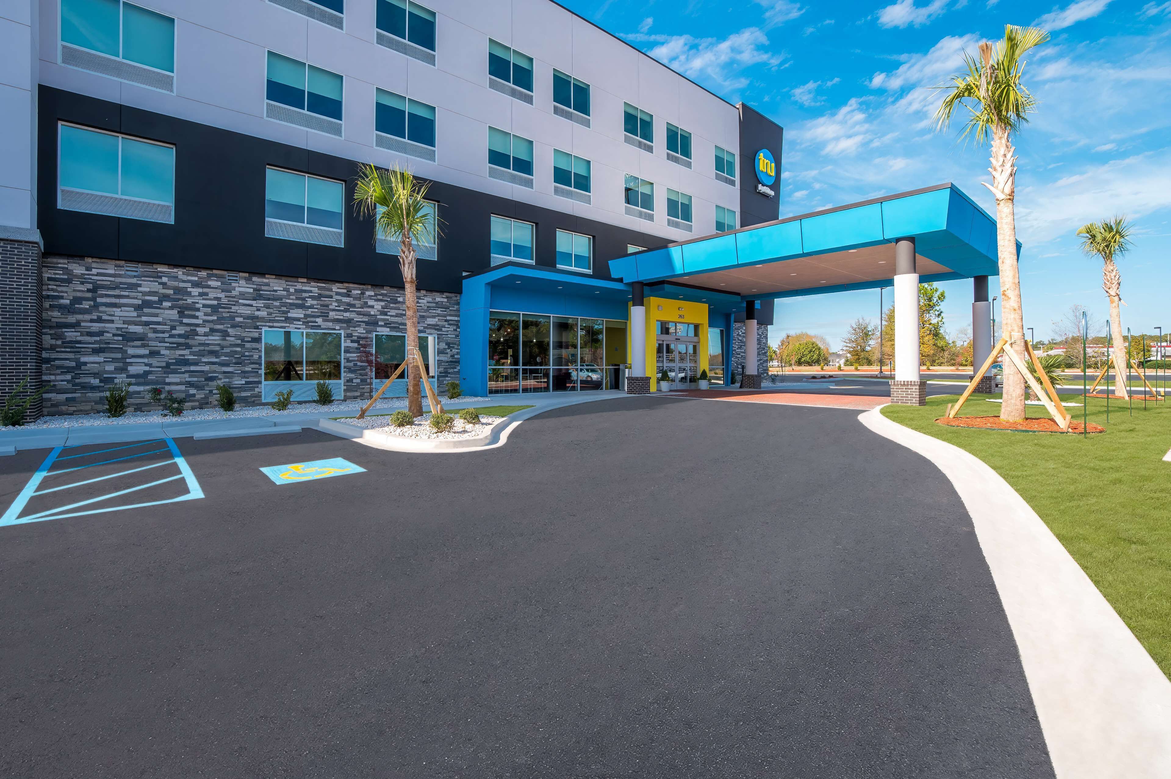 A modern hotel with a blue and white facade, a covered entrance, and a parking lot with marked handicapped spaces.
