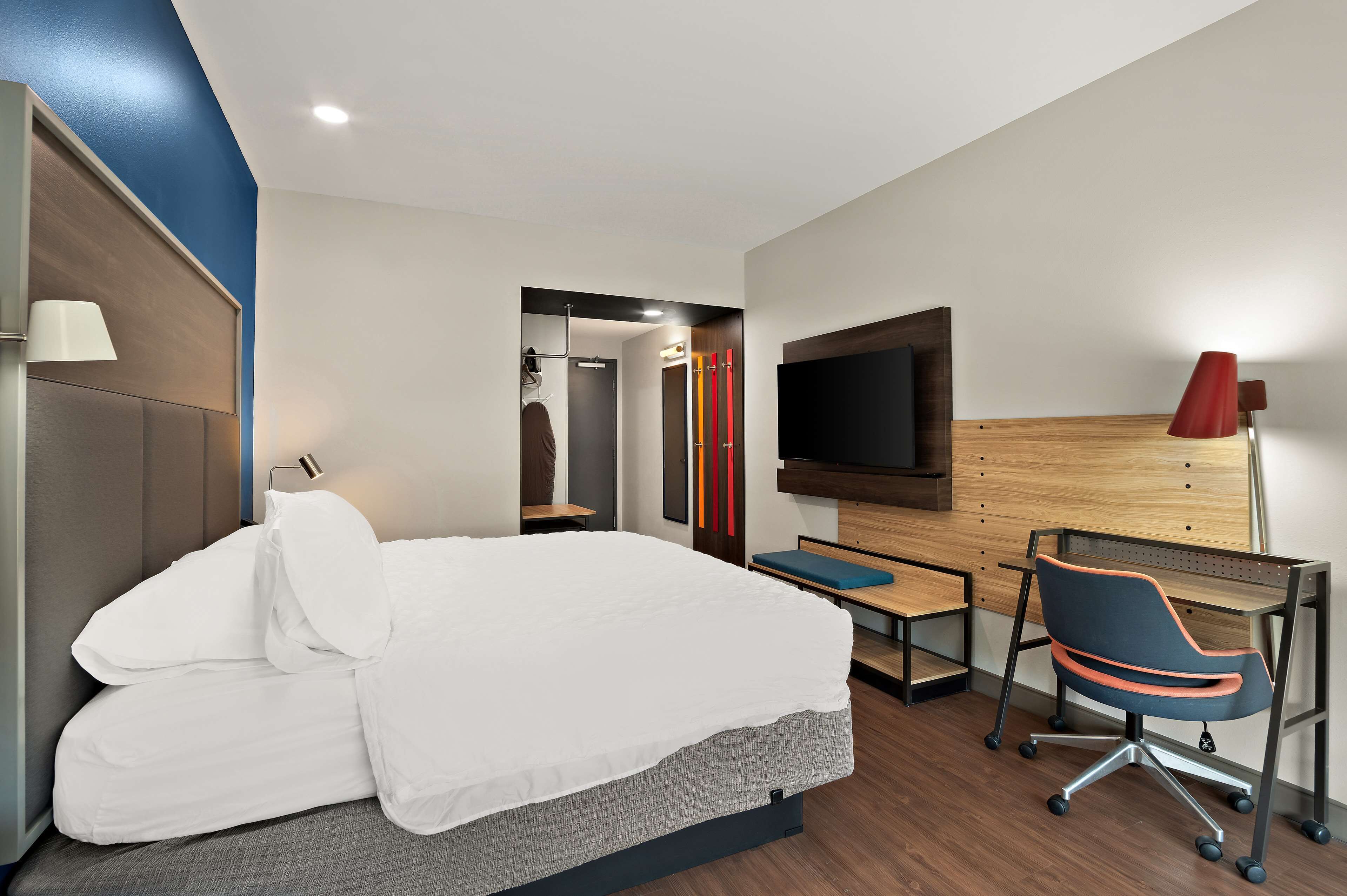 A modern hotel room with a bed, desk, chair, TV, and a mirror.