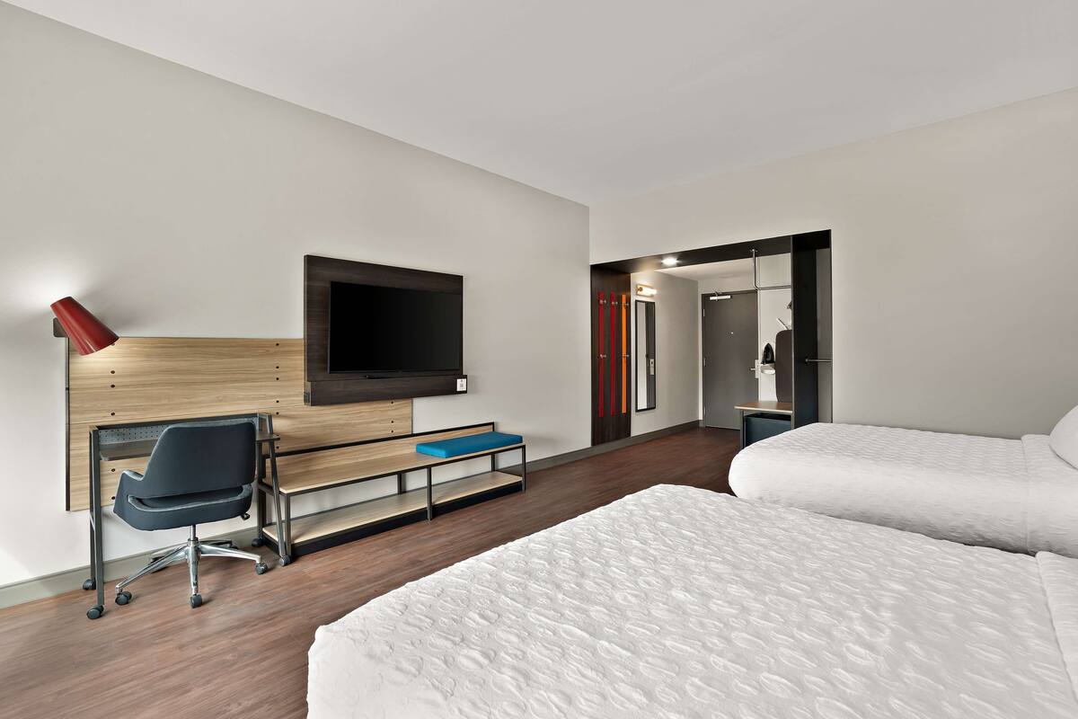 A hotel room with a bed, a desk with a chair, a TV mounted on the wall, and a mirror.