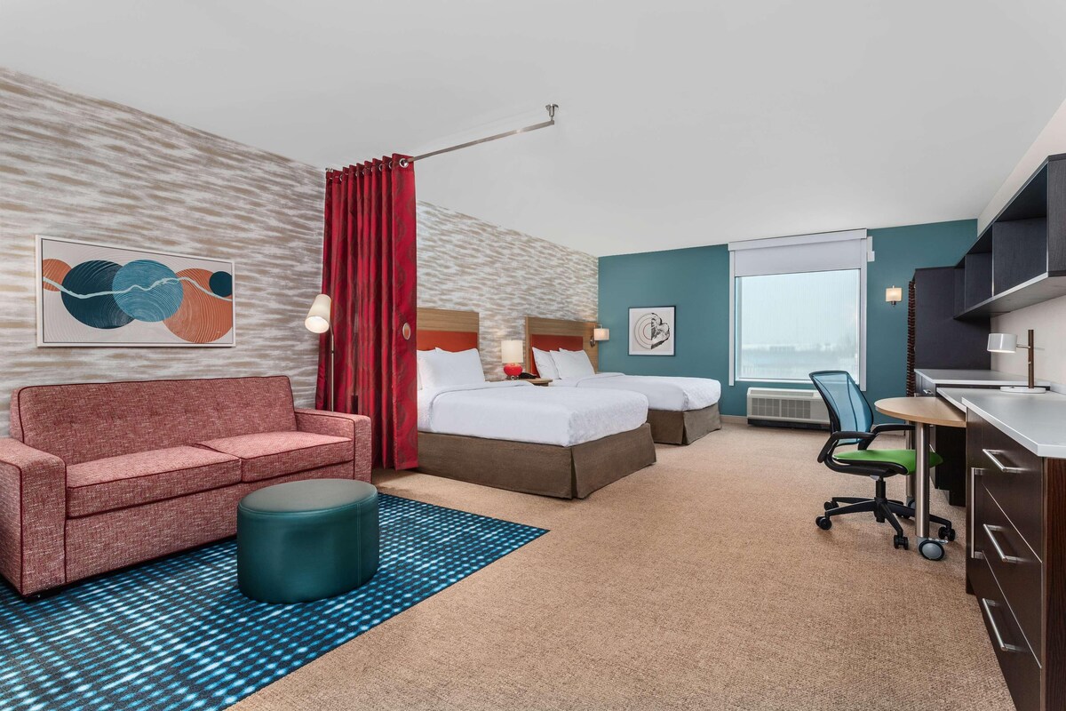 Habitación de hotel con sofá, dos camas, escritorio y una silla.