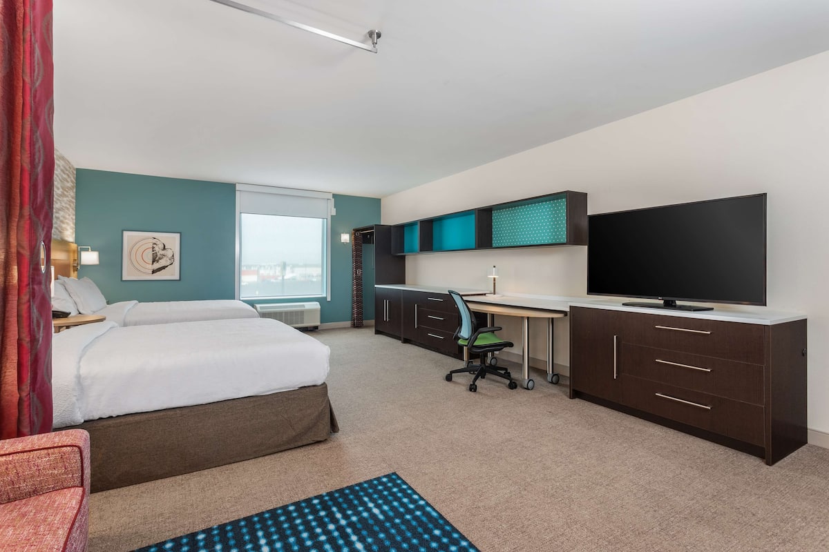 Habitación de hotel con cama, escritorio, silla, televisor y vista a la ciudad.