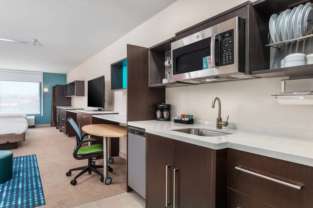 Habitación de hotel moderna con kitchenette, cama, escritorio y vista a la ciudad.