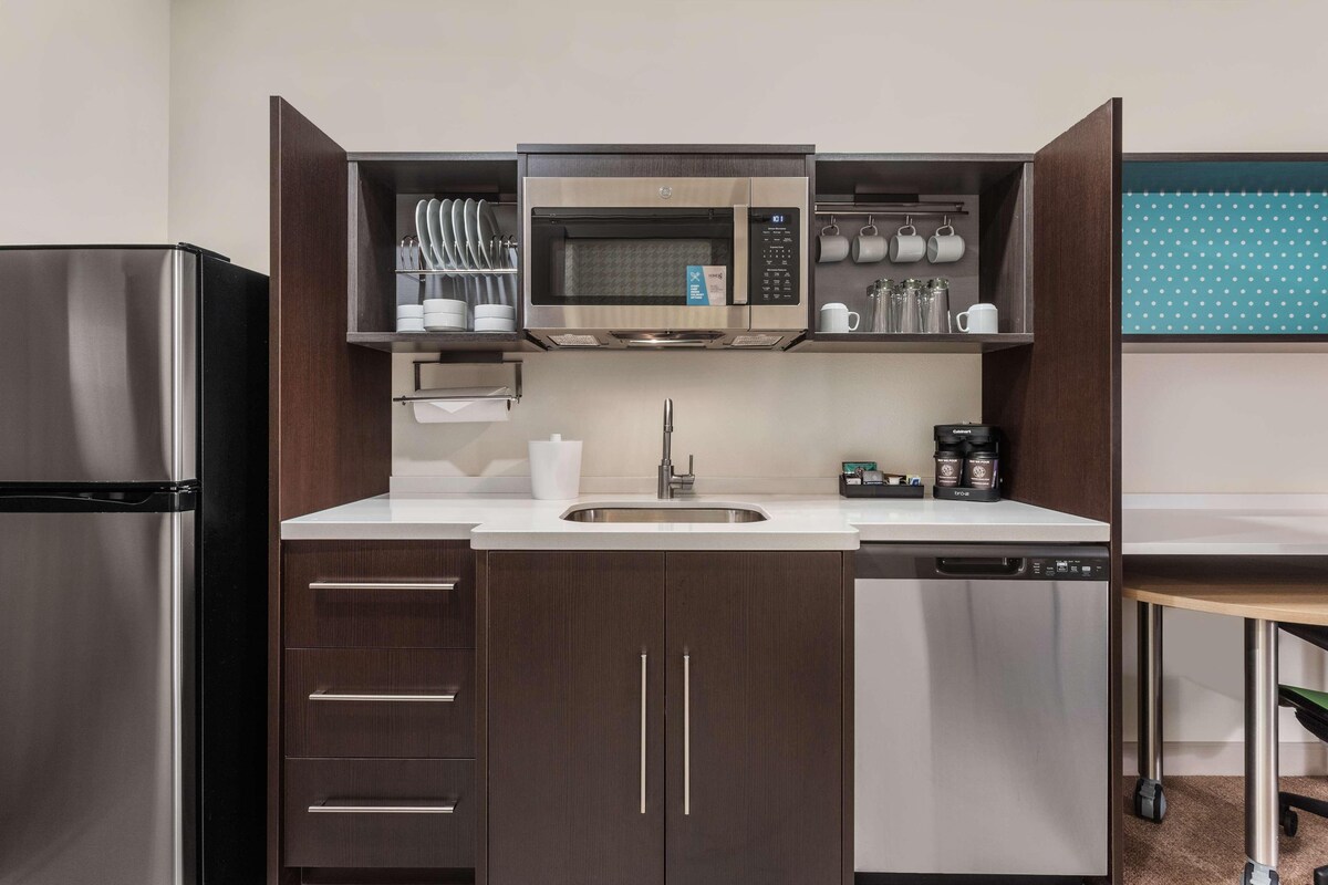 Cocina compacta con microondas integrado, refrigerador de acero inoxidable y lavavajillas.