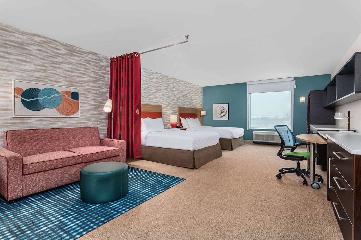 Habitación de hotel con sofá, dos camas, escritorio y una silla.