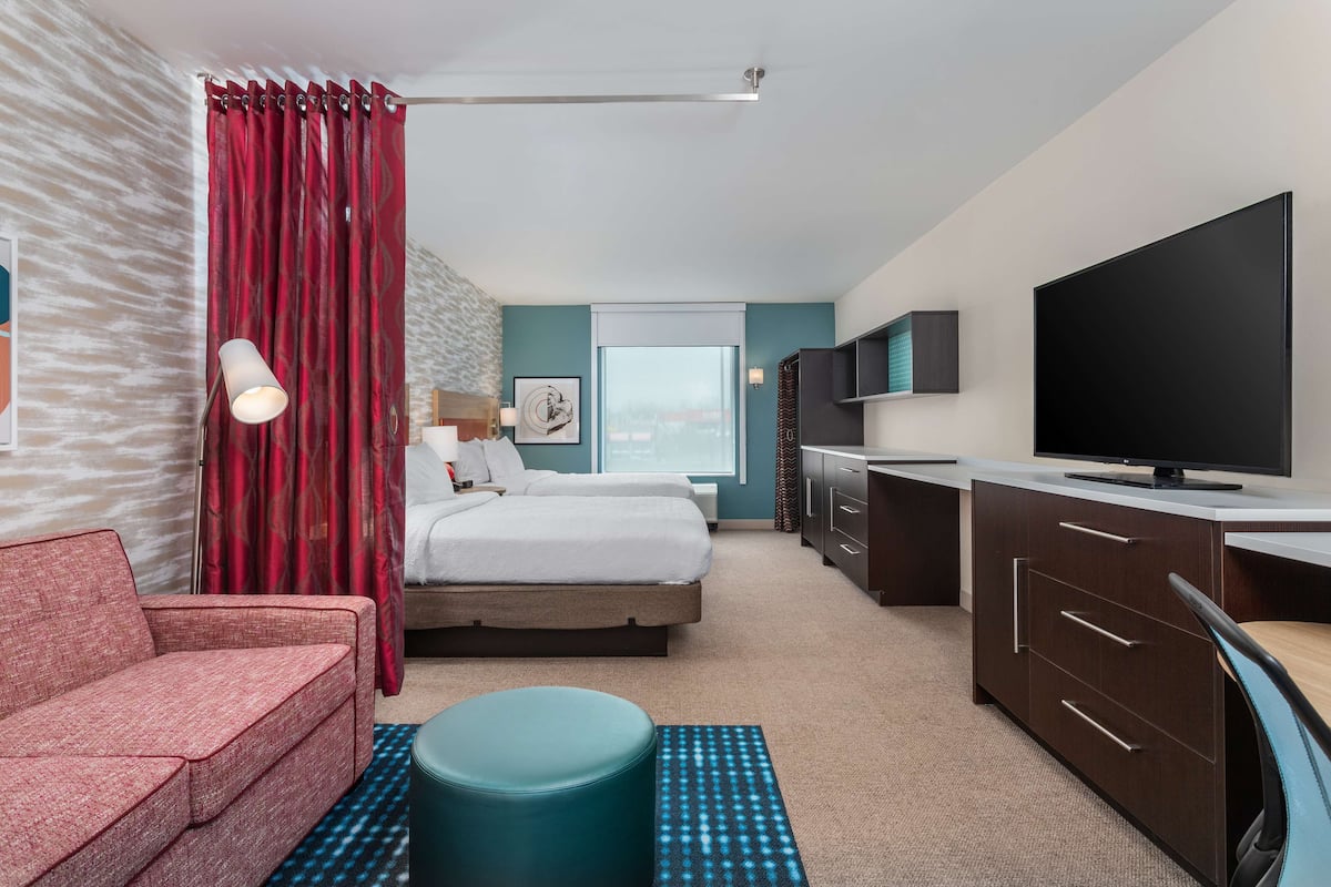 Una habitación de hotel con cama, escritorio, televisor, sofá y ventana con cortinas.