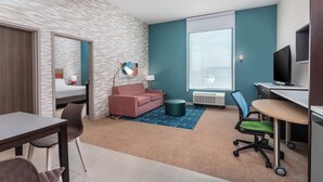 Una habitación de hotel moderna con kitchenette, un sofá, un escritorio y un ventanal grande.