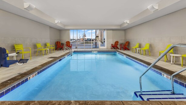 Una piscina interior con agua azul cristalina, sillas amarillas y rojas alrededor del borde, y vistas al exterior a través de amplias ventanas.