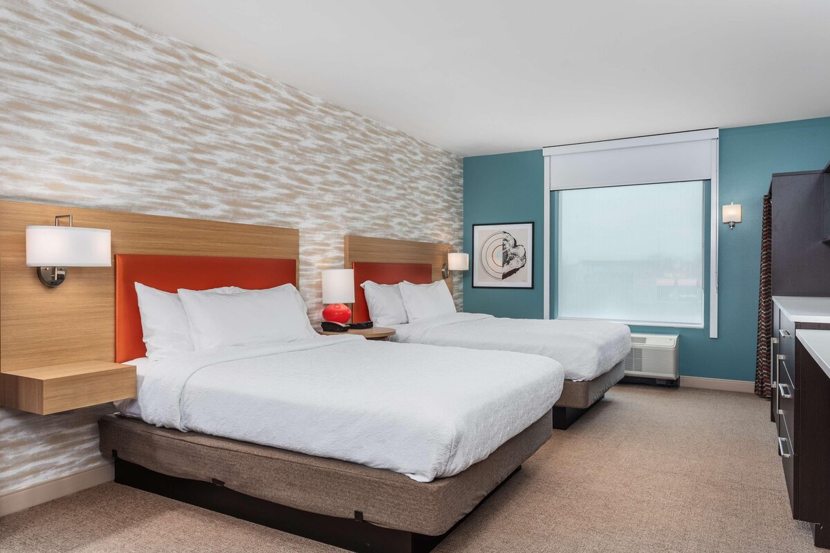 Habitación de hotel con dos camas, un ventanal grande y vistas a la ciudad.