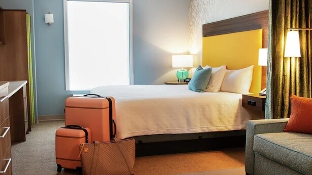 A hotel room with a bed, a desk, a chair, and a suitcase. - Home2 Suites By Hilton Newberry (Newberry)