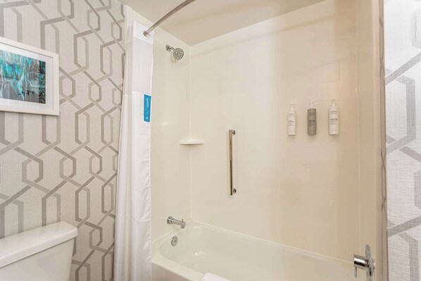 A bathroom with a shower, toilet, and three toiletry bottles on the wall.