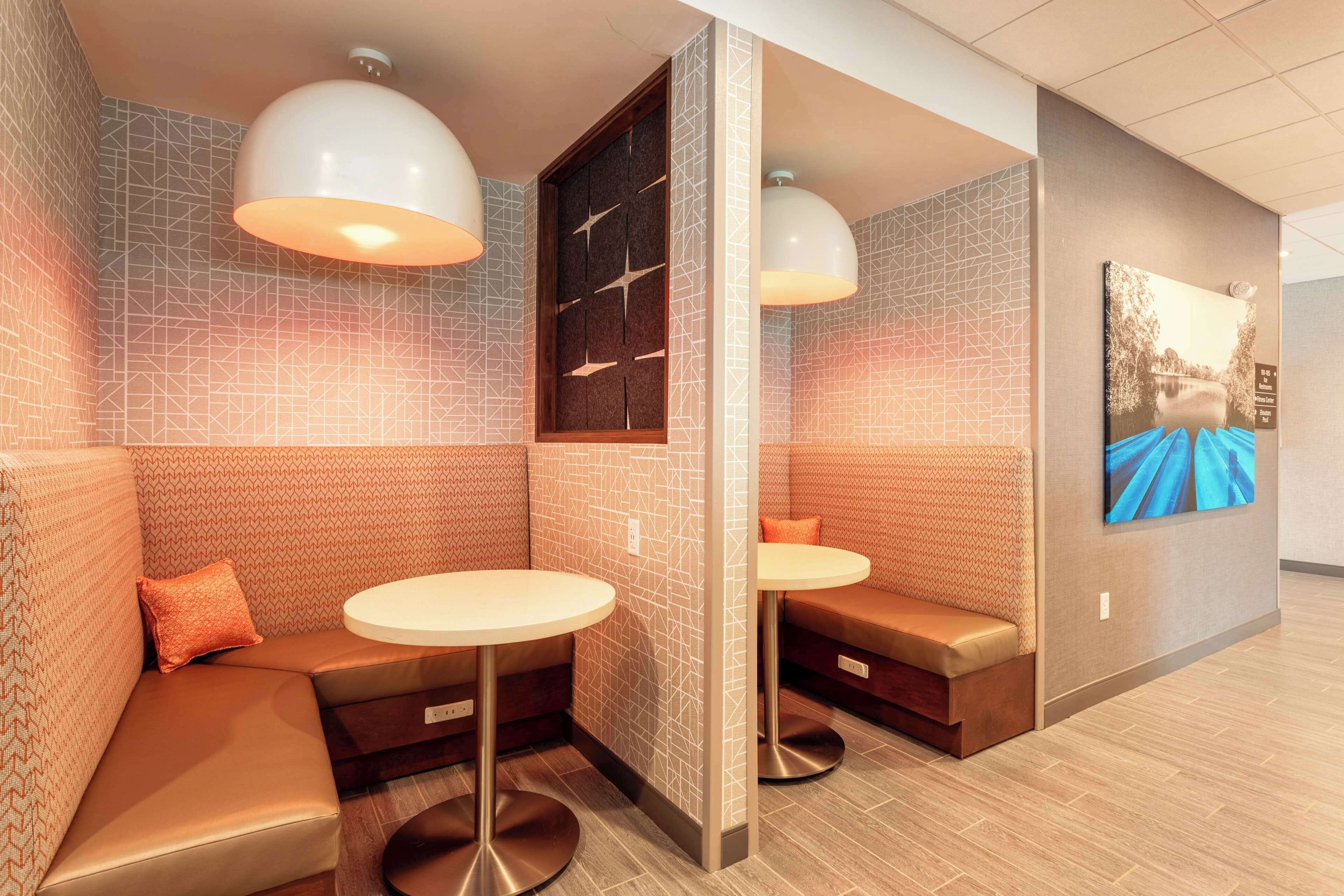 A modern lounge area with cushioned seating, pendant lighting, and a wall-mounted artwork.
