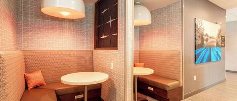 A modern lounge area with cushioned seating, pendant lighting, and a wall-mounted artwork.