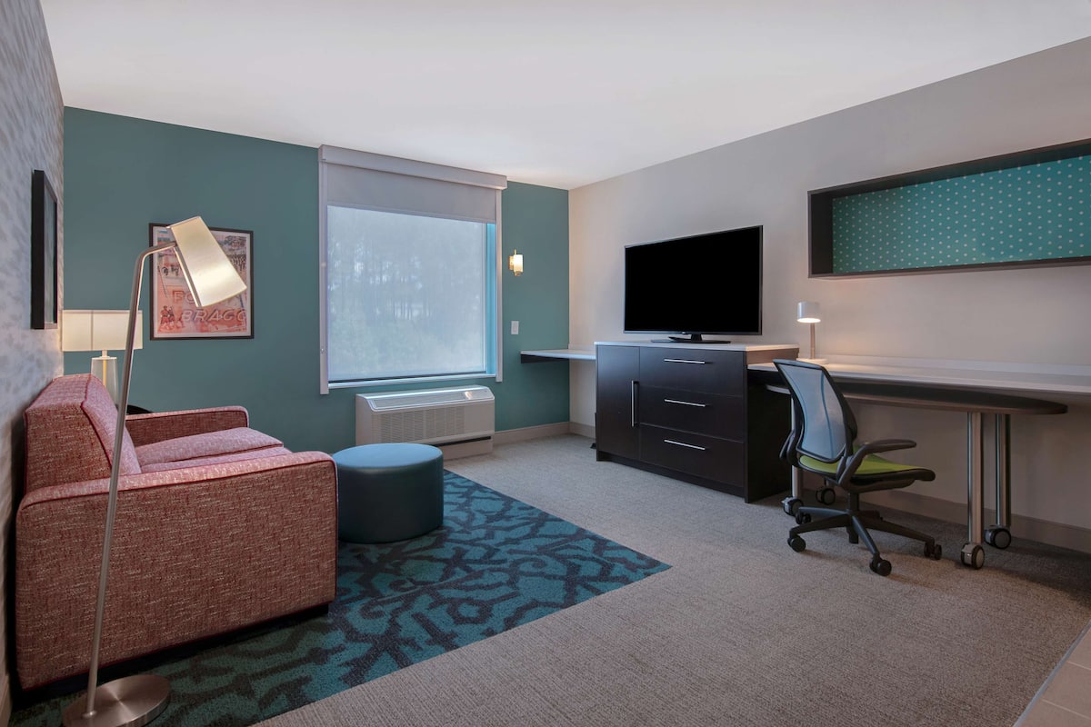 Habitación de hotel con sofá, escritorio, silla, televisión de pantalla plana y ventana grande.