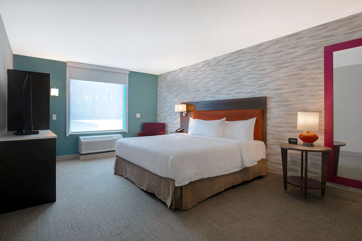 Una habitación de hotel con una cama grande, televisión, escritorio y ventana.