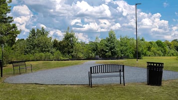 A park with a gravel path, benches, and a trash can.