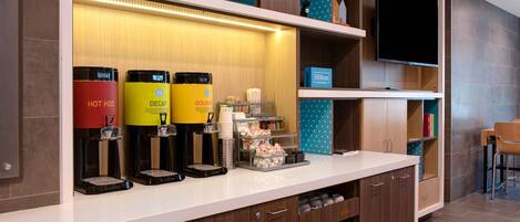 A hotel reception area with a coffee station, a flat-screen TV, and a seating area.