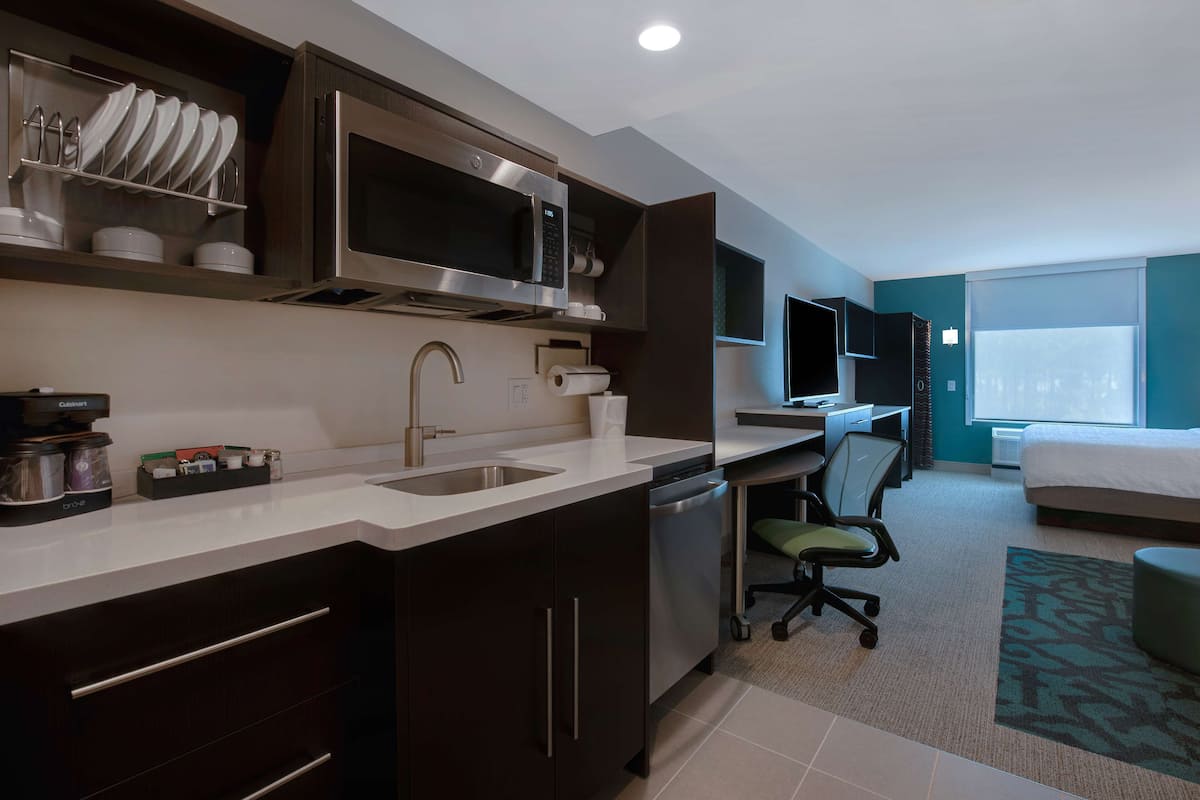 Una habitación de hotel moderna con kitchenette, una cama, un escritorio y un televisor.
