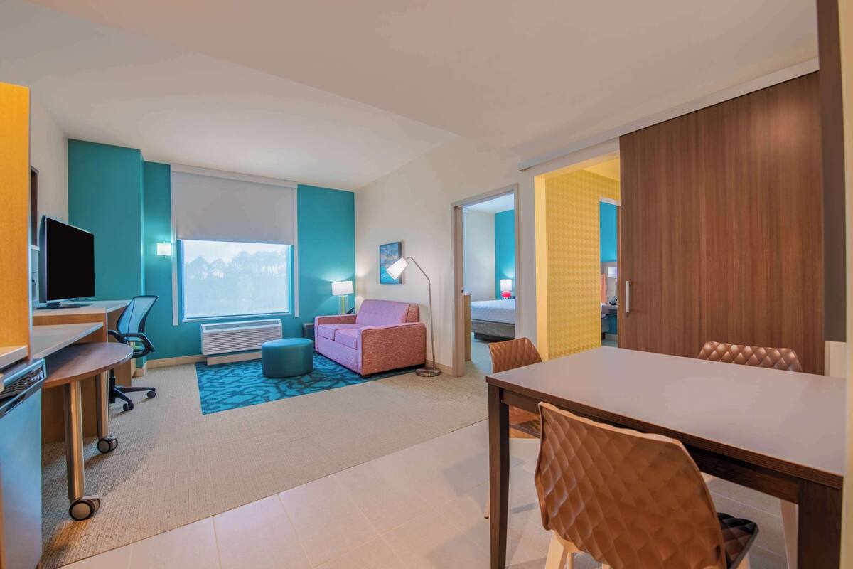 A modern hotel room with a desk, chair, sofa, and dining table.