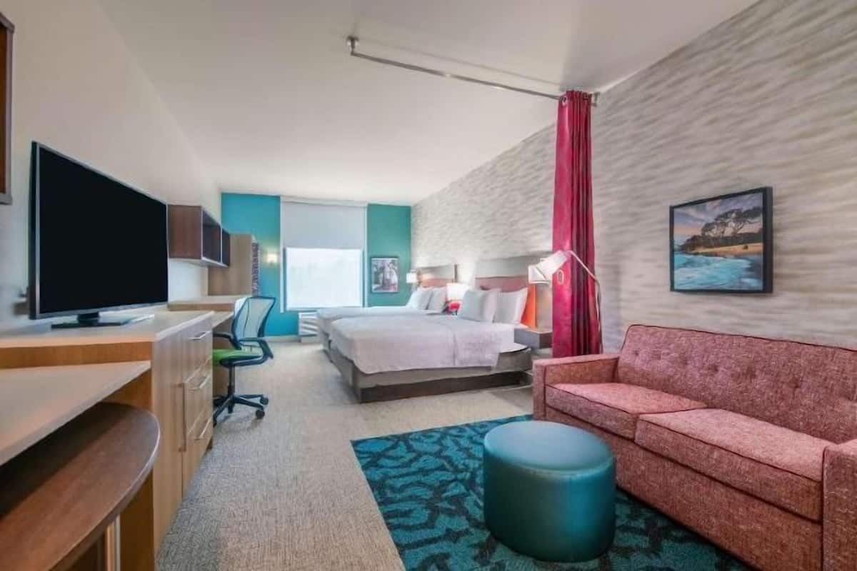 A hotel room with a bed, a desk with a TV, a sofa, a chair, and a window.