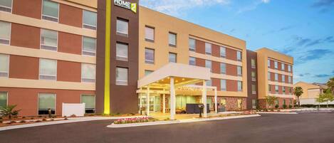 A modern hotel with a covered entrance, multiple floors, and a clear sky.