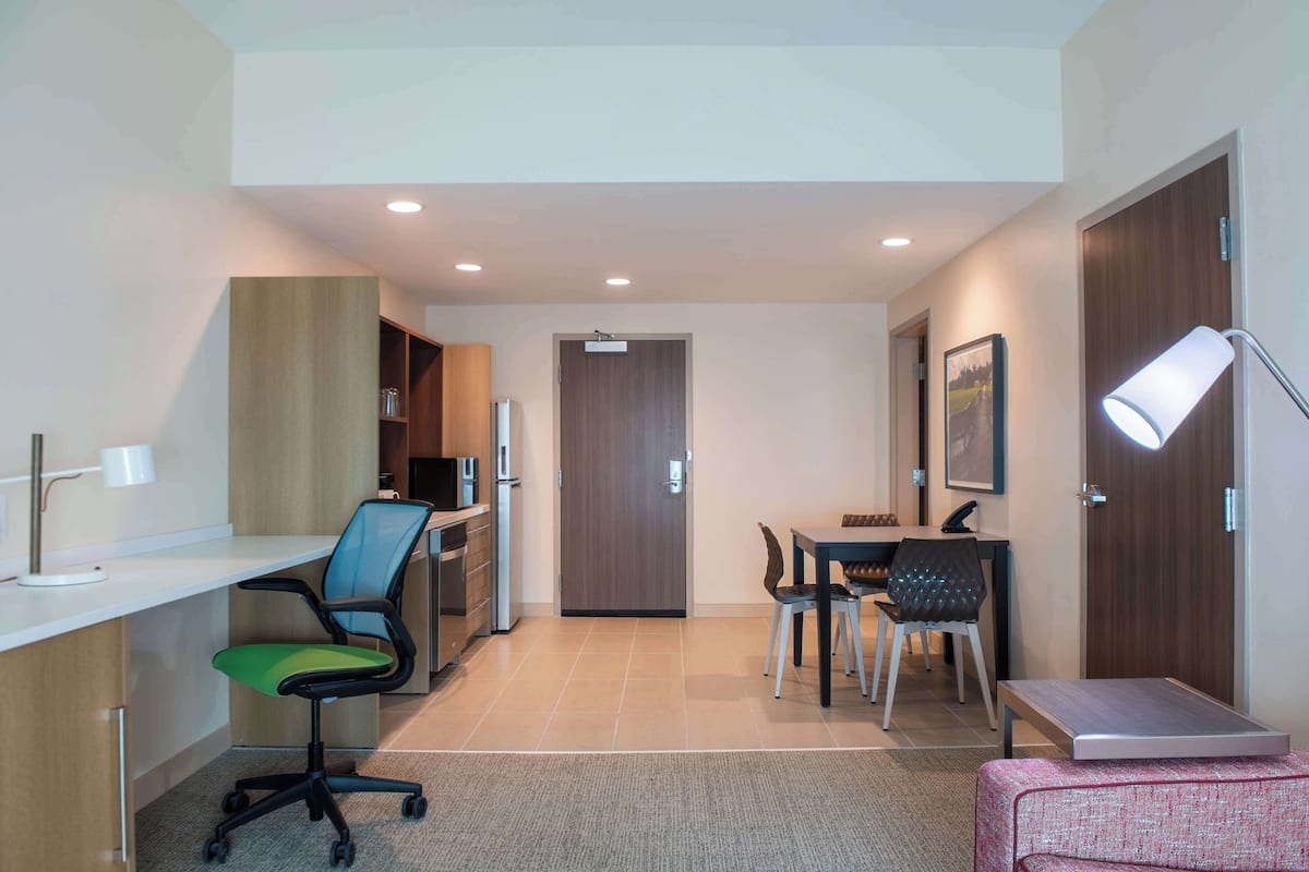 A modern hotel room with a desk, office chair, dining table, and chairs.