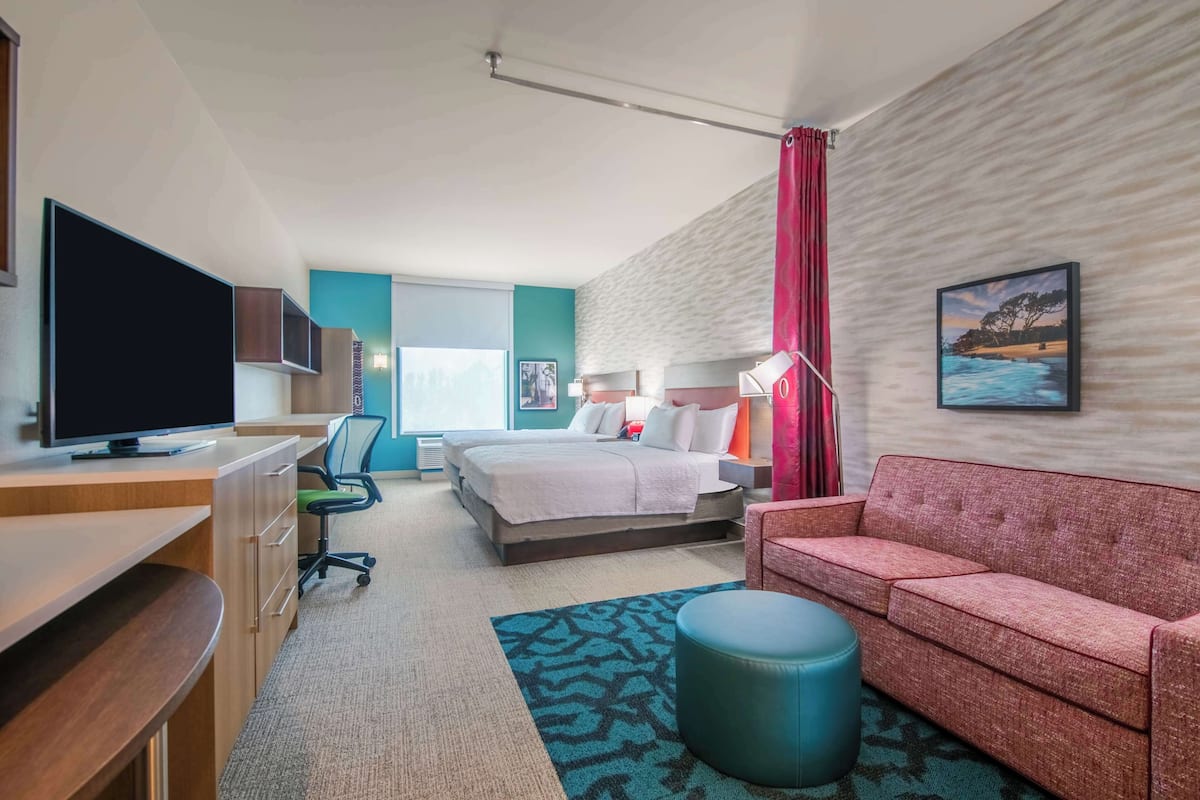A hotel room with a bed, a desk with a TV, a sofa, a chair, and a window with curtains.