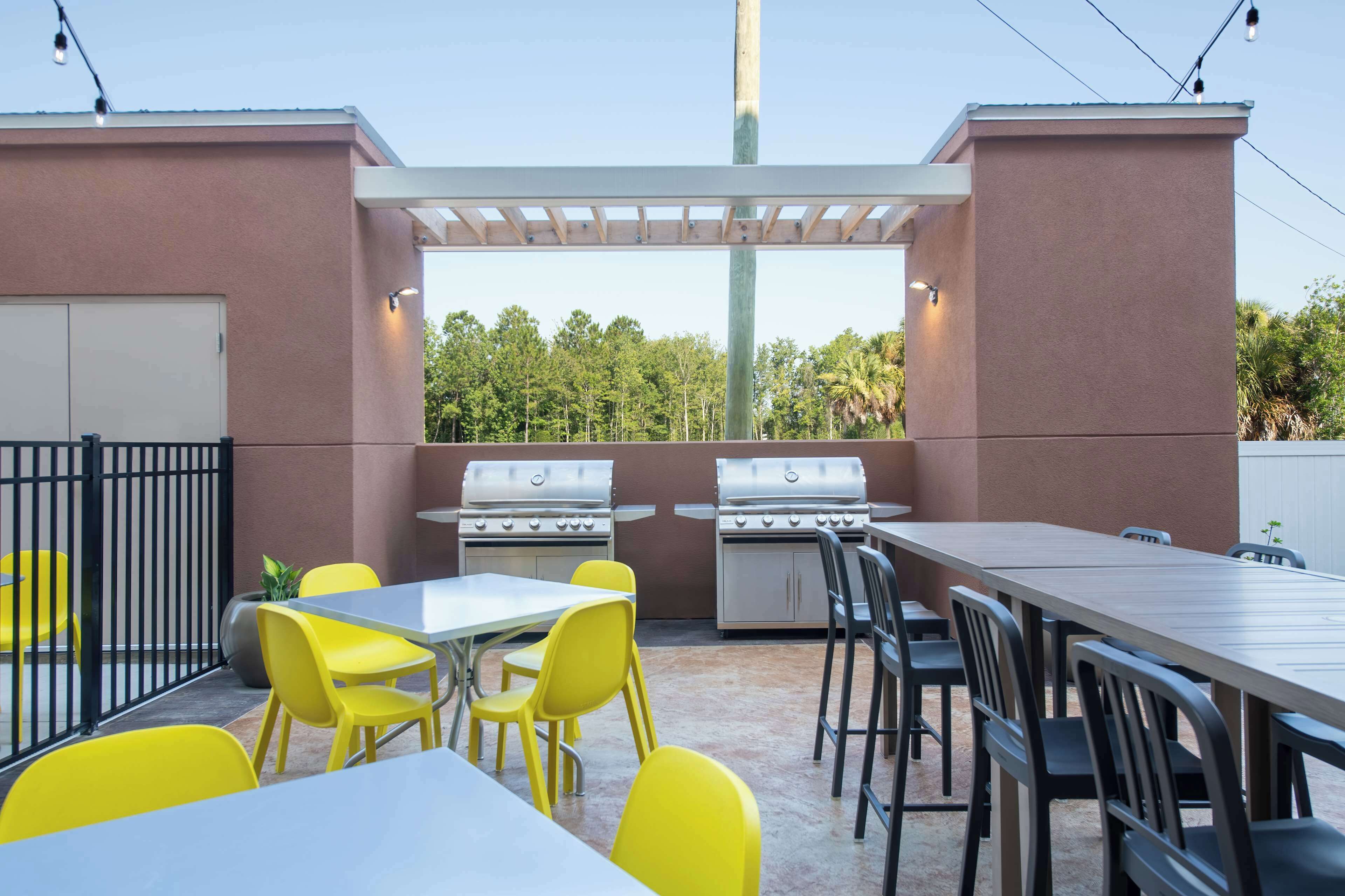 An outdoor patio with a table and chairs, two grills, and a pergola.