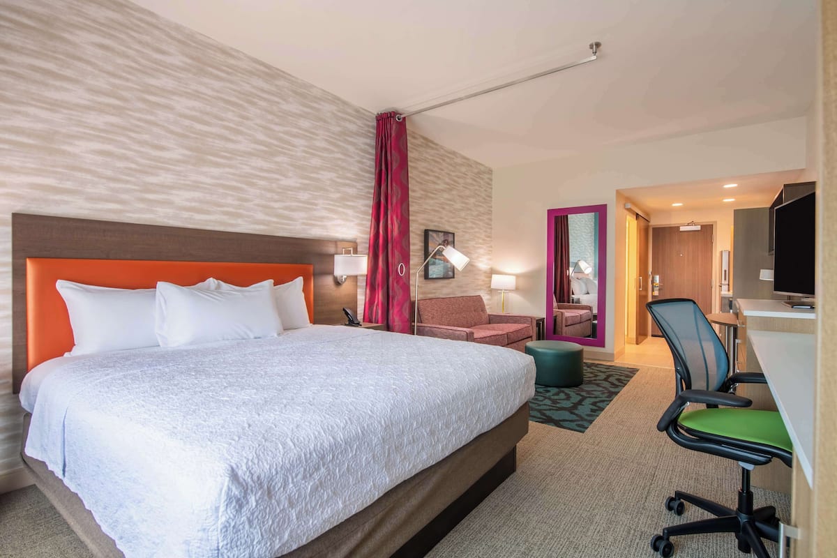 A hotel room with a large bed, a desk with a chair, a television, and a bathroom visible through an open door.