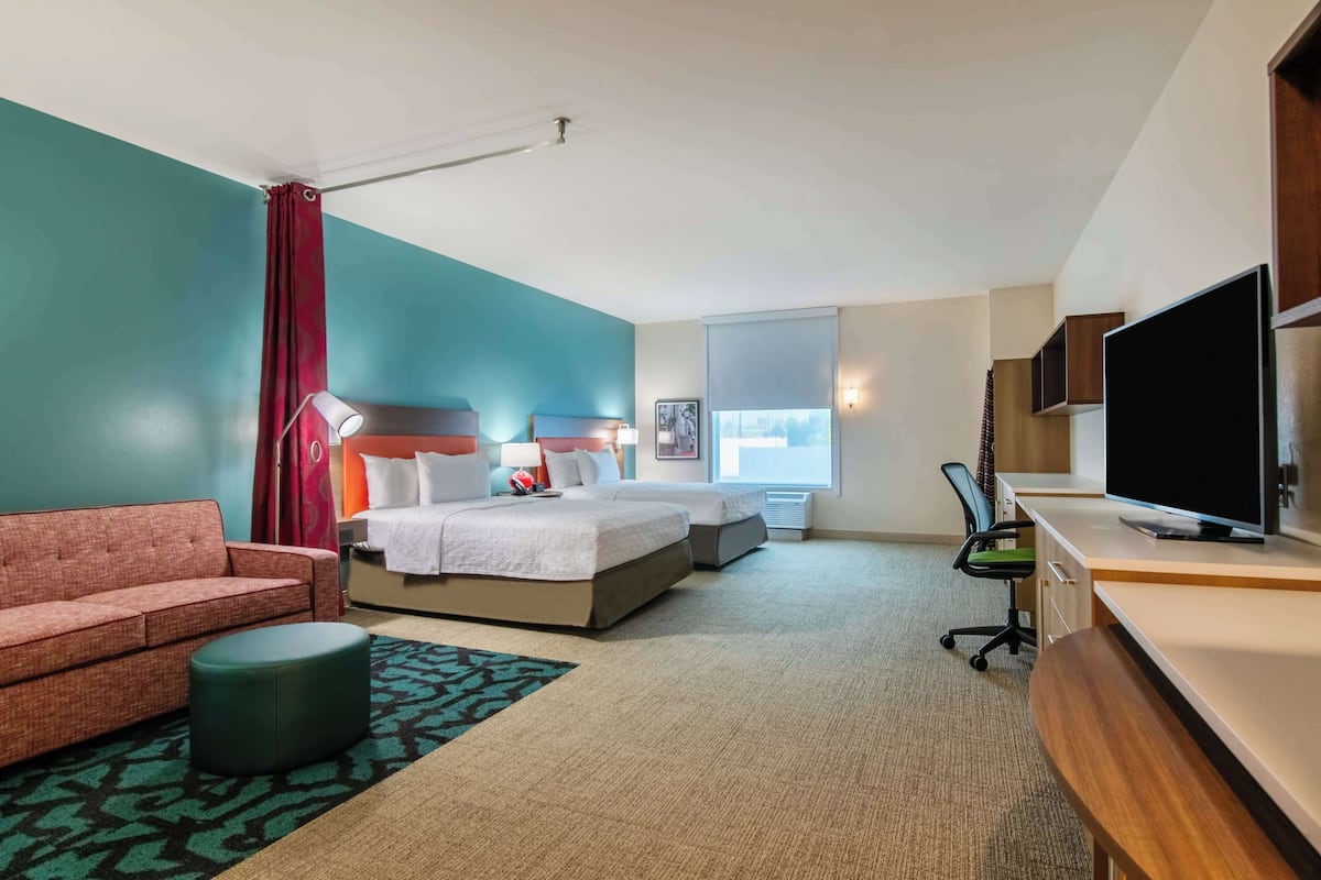 A hotel room with a bed, a desk, a TV, a sofa, and a window.